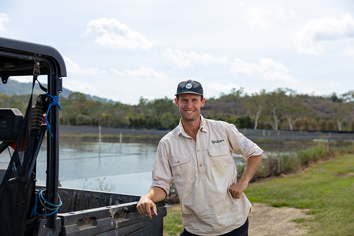 Nathan Cleasby leans on the back of a work buggy smiling at the camera