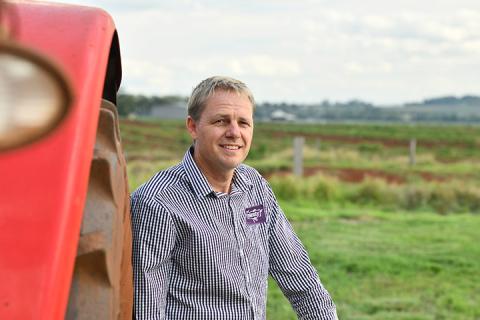 Man leans on red tractor with green fields behind him