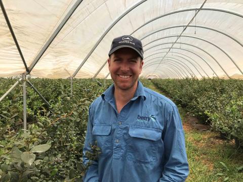 A man stands in a greenhouse smiling at the camera