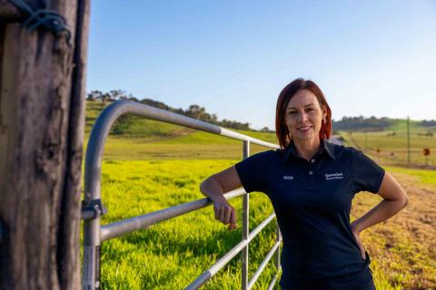 A young woman, leaning on a gate, smiles at the camera